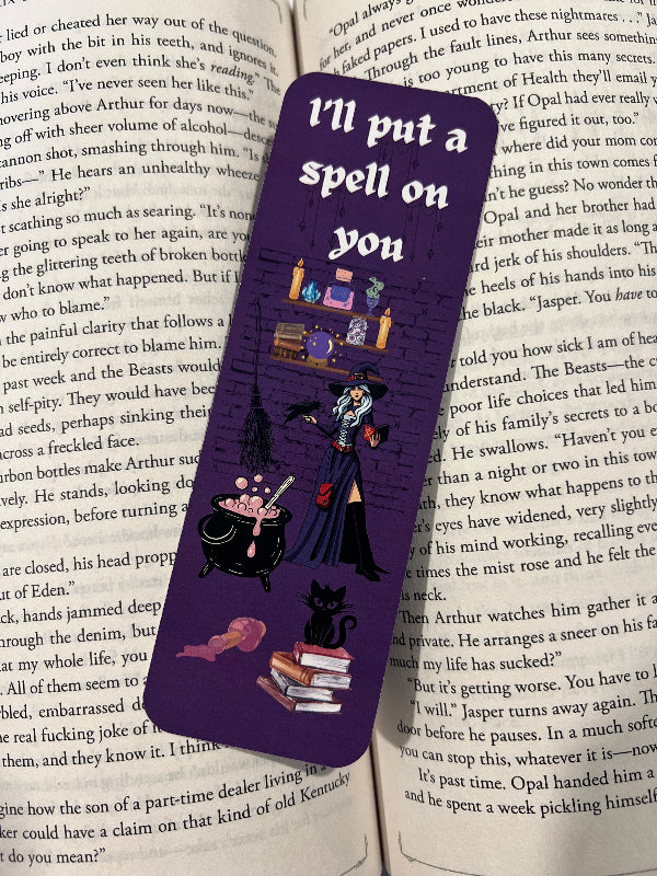 Purple bookmark with witch illustration and text 'I'll put a spell on you' on an open book.