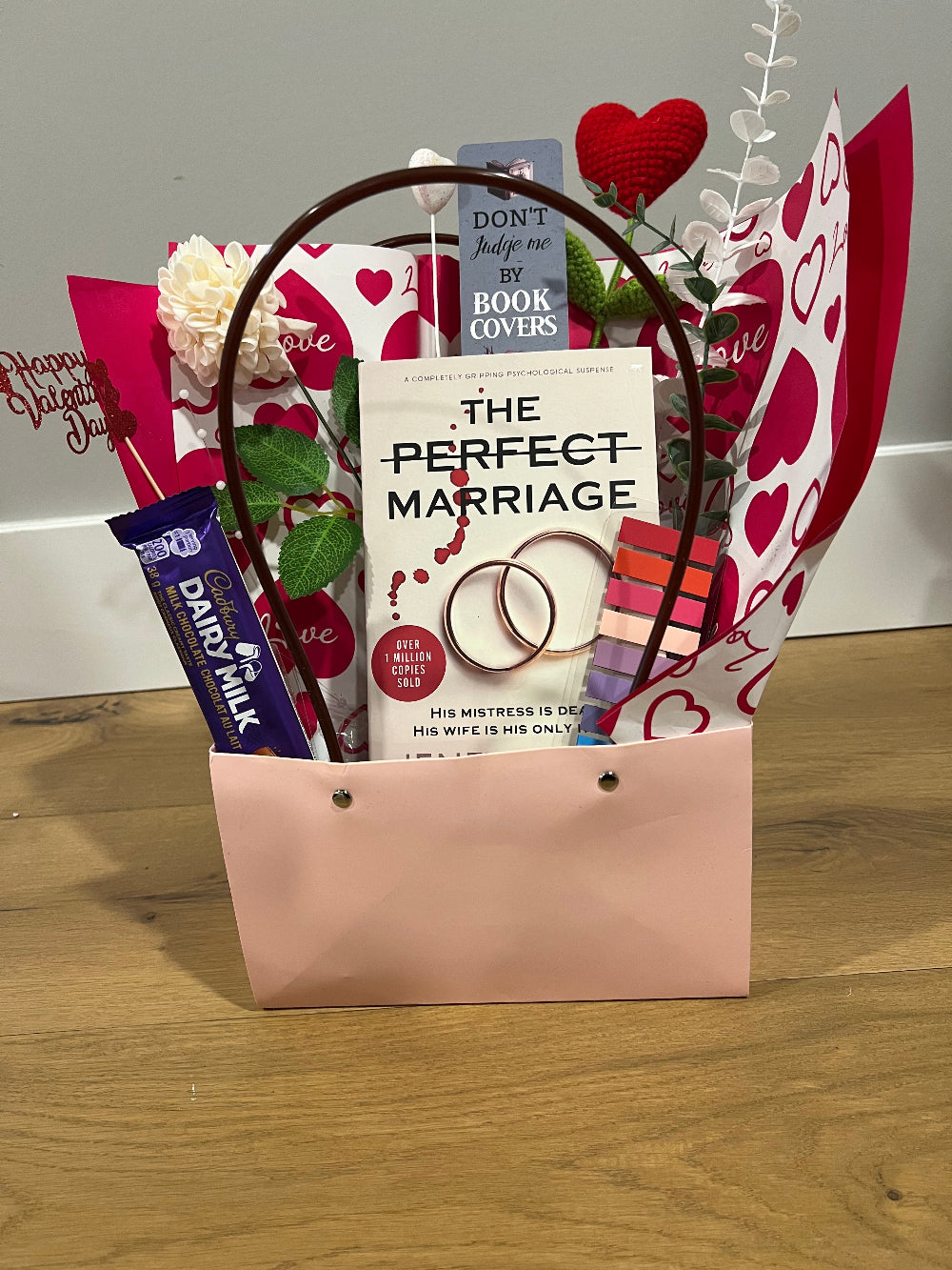 Valentine's Day gift basket with books, chocolate, and decorative items on a wooden surface.