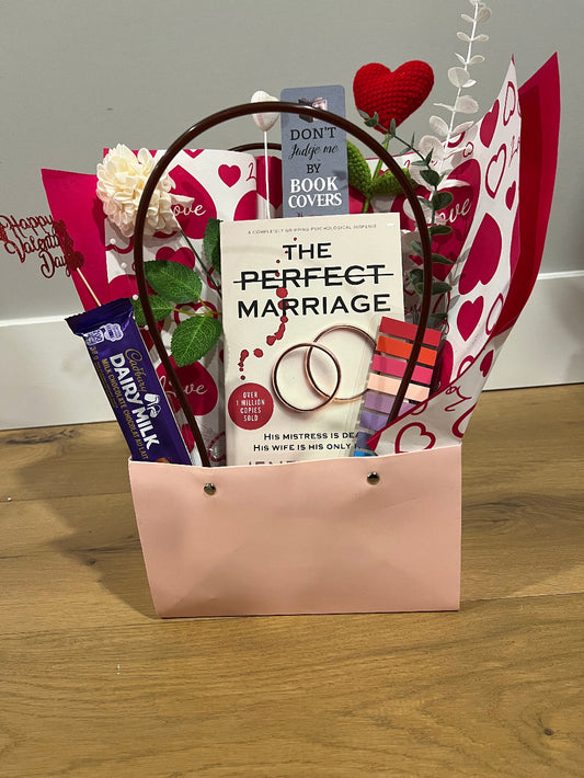 Valentine's Day gift basket with books, chocolate, and decorative items on a wooden surface.