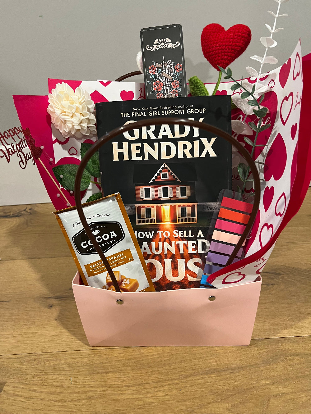 Gift bag with items including a book, makeup, and a phone case on a wooden surface.
